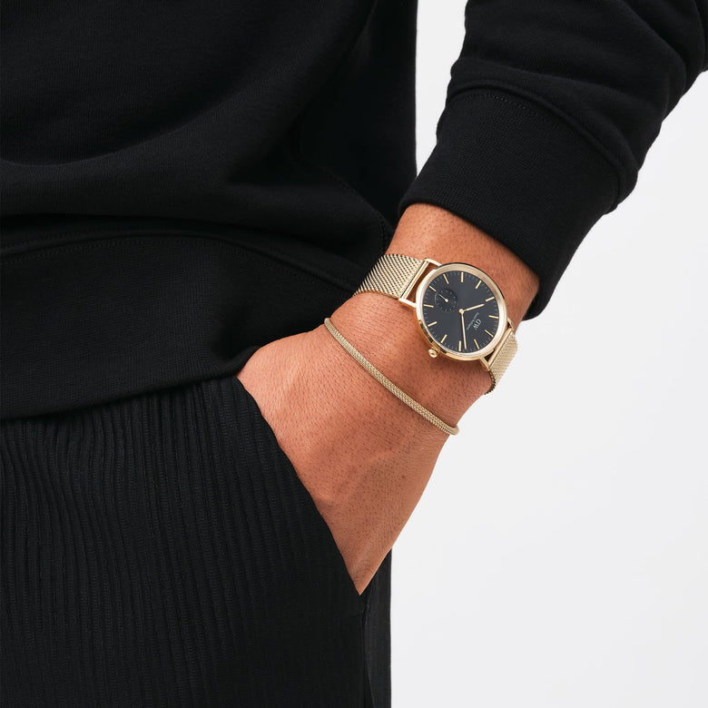 The Tide Mesh Bracelet Evergold 2.8 is worn on the wrist alongside a gold mesh watch, showcasing its slim gold mesh design and minimalist style paired with casual black clothing.