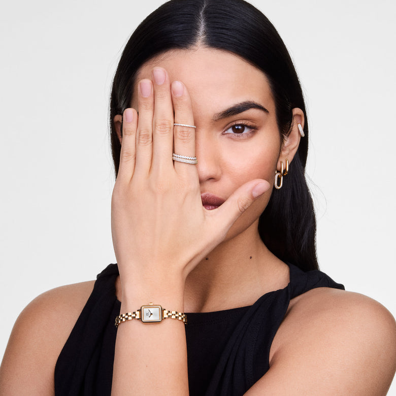 Quadro Mini Arch 3-link White Sunray Gold ladies watch worn on the wrist, showing its petite rectangular gold case, minimalist white sunray dial, and polished 3-link gold bracelet styled with a sleeveless black top.