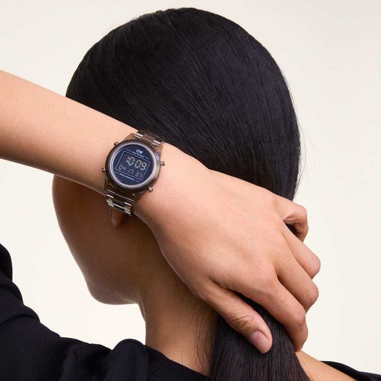 A person wearing the Daniel Wellington Retro Digital Dark Brown Dark Brown watch, showing its transparent dark brown link strap and round digital display with chronograph features, styled for everyday wear.