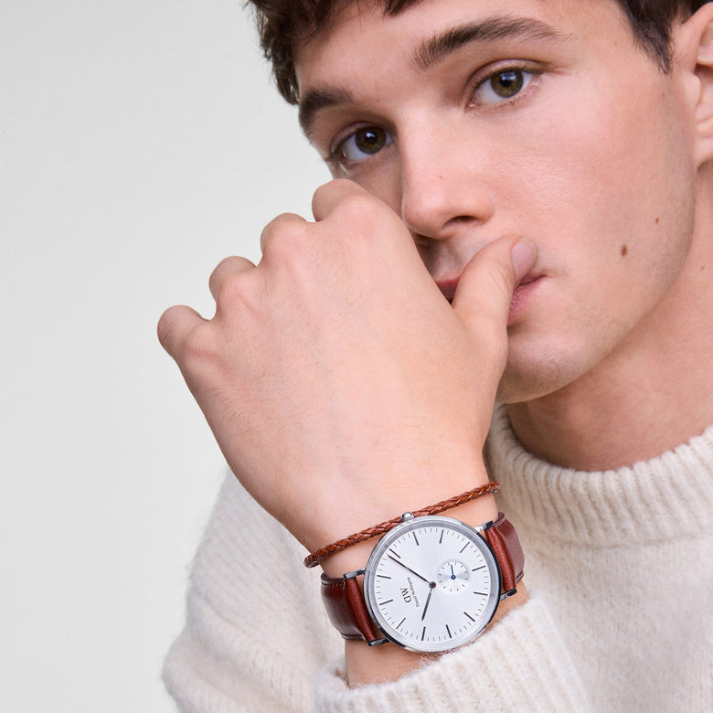 A man wearing the Classic Multi-Eye St Mawes Off-white Sunray Silver watch with a brown leather strap and silver case, styled alongside a braided bracelet and a cream knit jumper for a relaxed, everyday look.