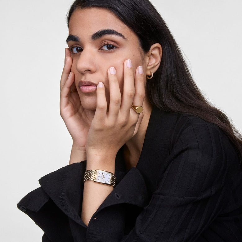 Classic Signet Ring Gold worn on the hand, showcasing its polished, minimalist design and broad gold surface paired with a stylish black outfit.