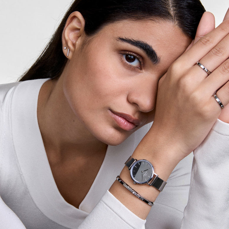 A woman wearing the Petite Reflection & Classic Lumine Bracelet Silver Set, featuring a silver mesh watch with a minimalist dial and a slim silver bracelet with diamanté details, styled with matching rings and a white top for a modern, elegant look.
