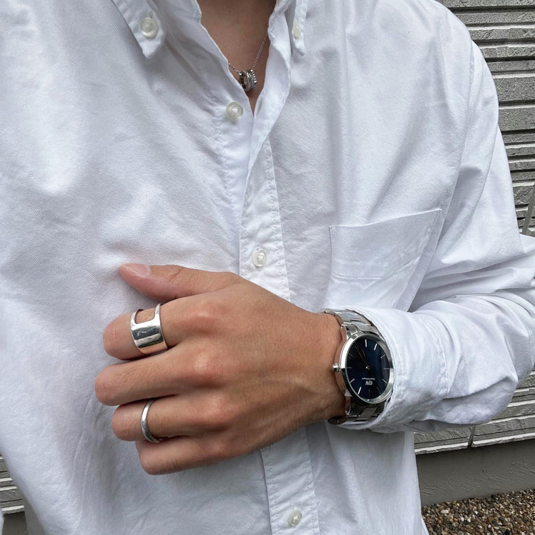 Daniel Wellington Iconic Link watch with a silver stainless steel bracelet and black dial, worn with a crisp white shirt and silver rings for a smart-casual look.