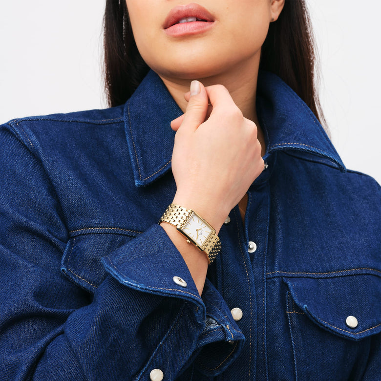A woman wearing the Bound 9-Link Gold watch with a rectangular gold case and white dial, styled with a blue denim shirt for a modern, everyday look.