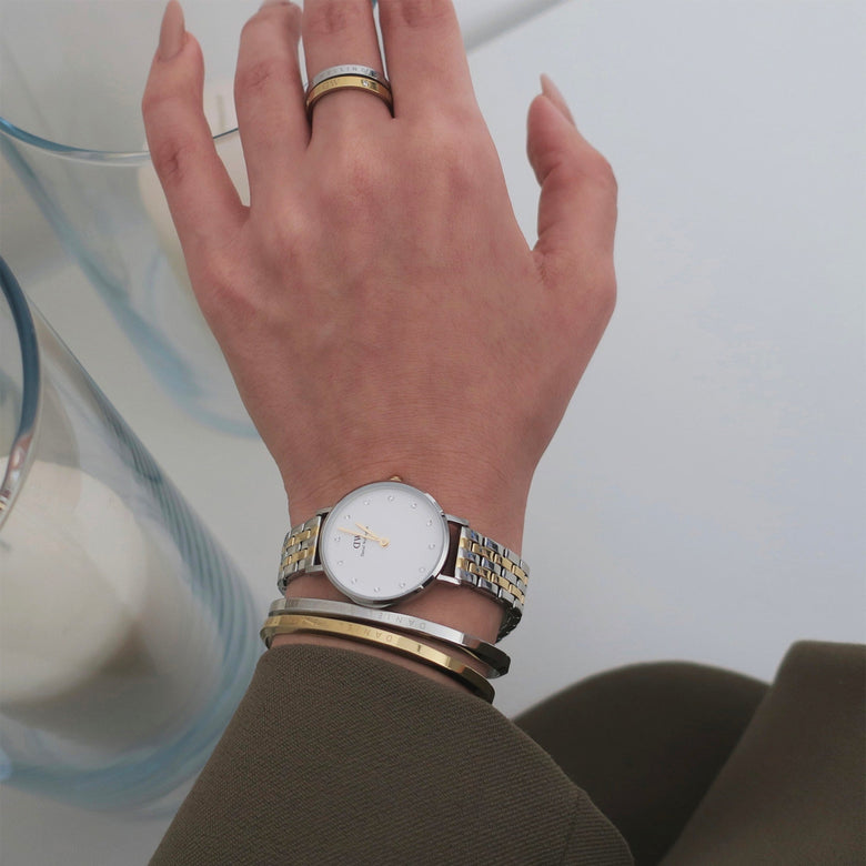 A woman wearing the Petite Lumine 5-link two-tone watch with a slim silver and gold bracelet, eggshell white dial and crystal markers, styled alongside gold and silver bangles for a chic, everyday look.