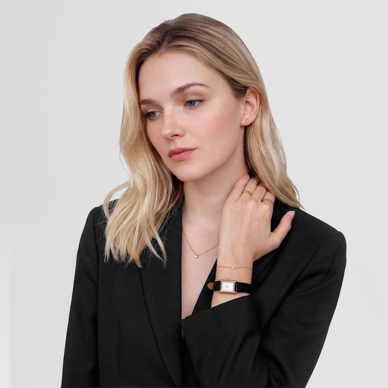 A woman wearing the Mirelle Solitaire Necklace Gold, styled with a black blazer and matching gold jewellery, showing the necklace’s delicate chain and petite cubic zirconia pendant resting elegantly along her neckline.