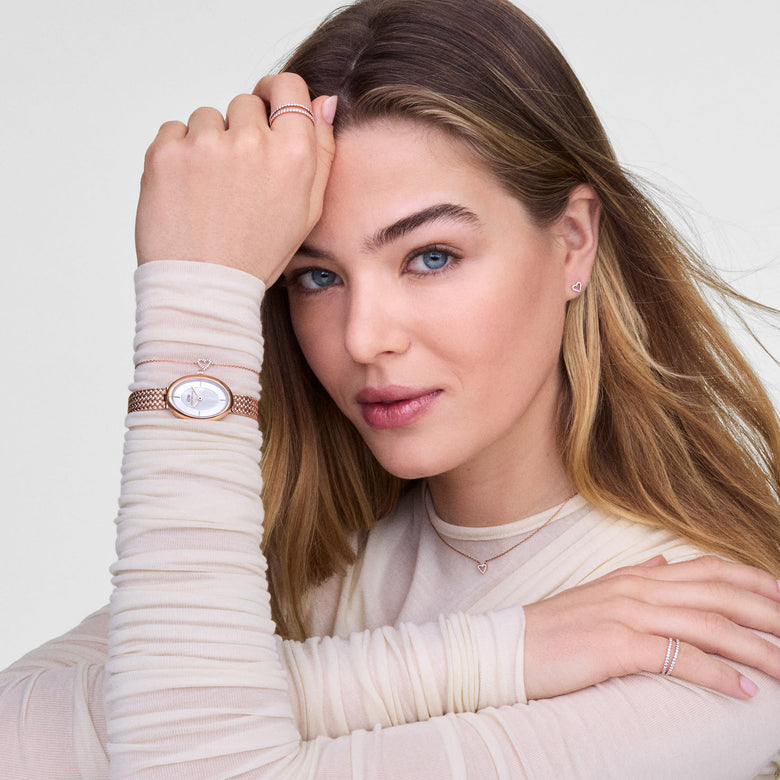 Juliette Braided Mesh White Sunray Rose Gold watch styled on a woman's wrist, showcasing the oval case, white sunray dial, and braided rose gold mesh strap paired with matching jewellery for a modern, minimalist look.