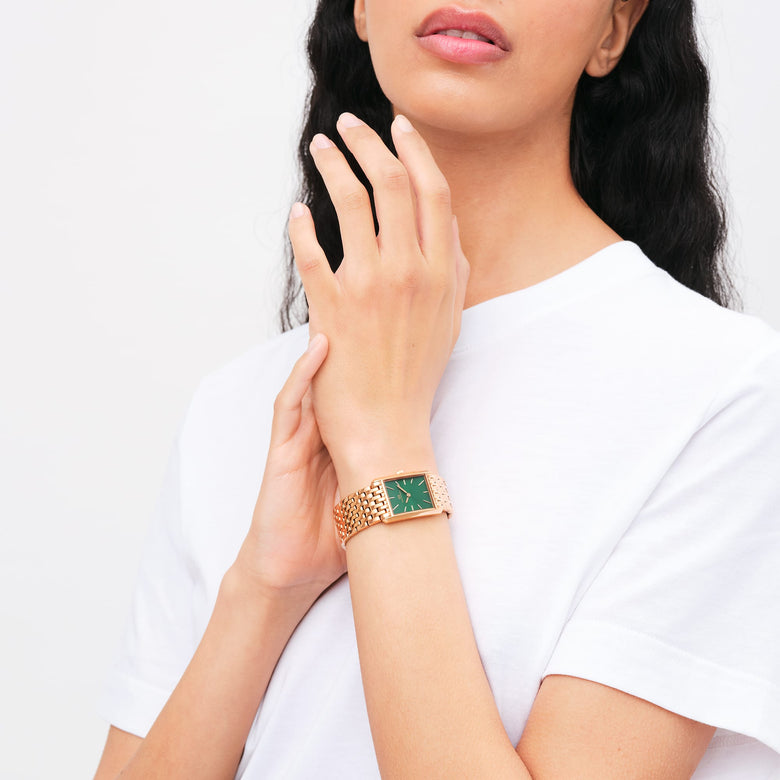 A woman wearing the Bound 9-Link Emerald Sunray ladies watch, featuring a rectangular rose gold case and bracelet with a green sunray dial, styled casually with a white top.