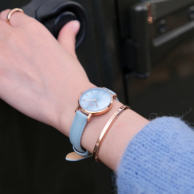 Petite Bluebell ladies watch with a pastel blue leather strap and rose gold case, worn on the wrist alongside a rose gold bangle, highlighting its elegant and versatile style for everyday wear.