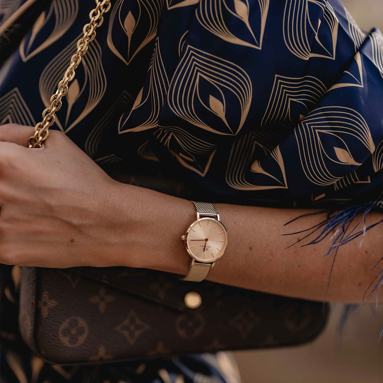 Petite Unitone Rose Gold watch with a rose gold mesh strap worn on a woman's wrist, styled with a patterned blouse and a gold chain handbag for a sophisticated, everyday look.