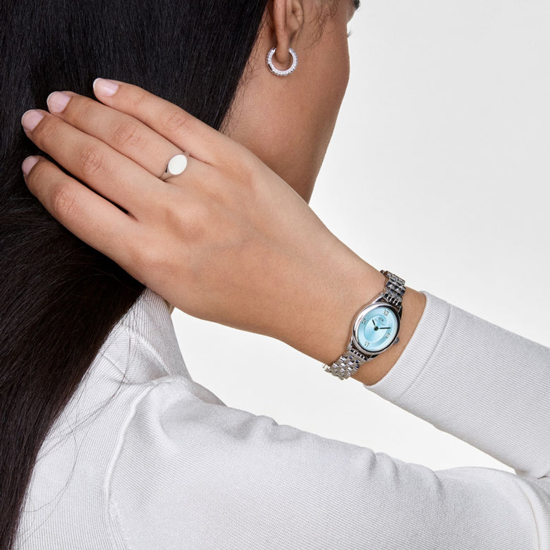 A woman wearing the Ophelia Mini Ice Blue Silver watch, showcasing its petite oval case, polished silver bracelet, and striking ice blue sunray dial with Roman numerals, styled with a white top and minimal jewellery for a modern, elegant look.