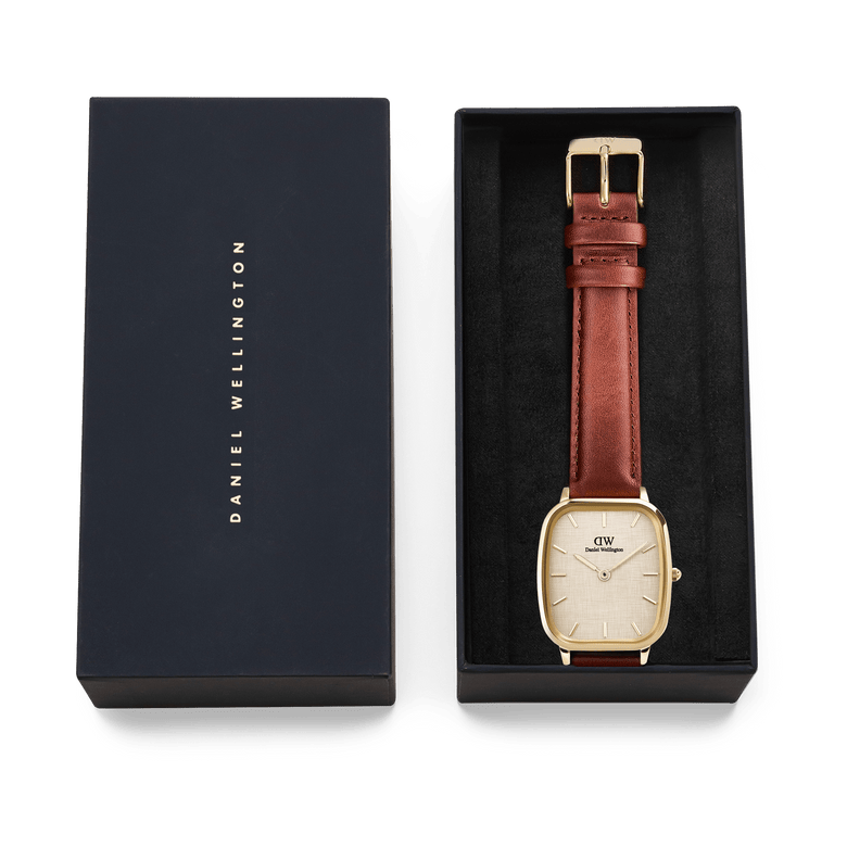 Daniel Wellington Marlon St Mawes Linen Gold men’s watch presented in a branded gift box, featuring a gold cushion-shaped case, linen-textured dial, and brown leather strap.