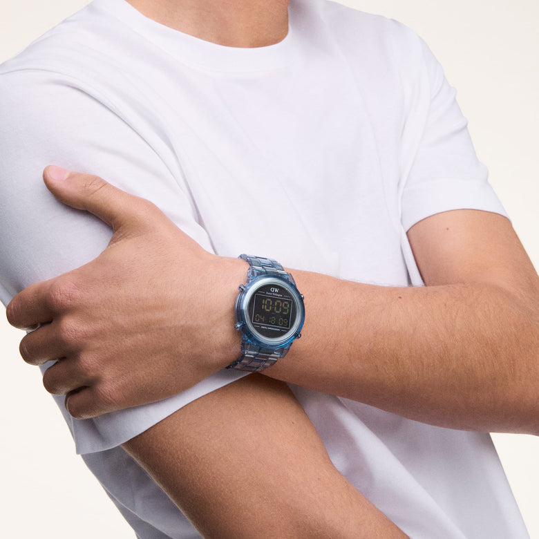 A man wearing the Retro Digital Light Blue Light Blue watch from Daniel Wellington, showing its transparent light blue link bracelet and bold black digital dial, styled casually with a white T-shirt.