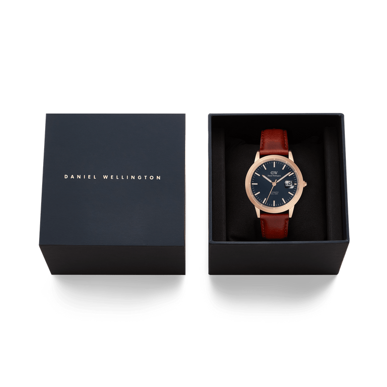 Iconic St Mawes Automatic Rose Gold watch with a blue enamel dial and brown leather strap, presented in a branded Daniel Wellington gift box.