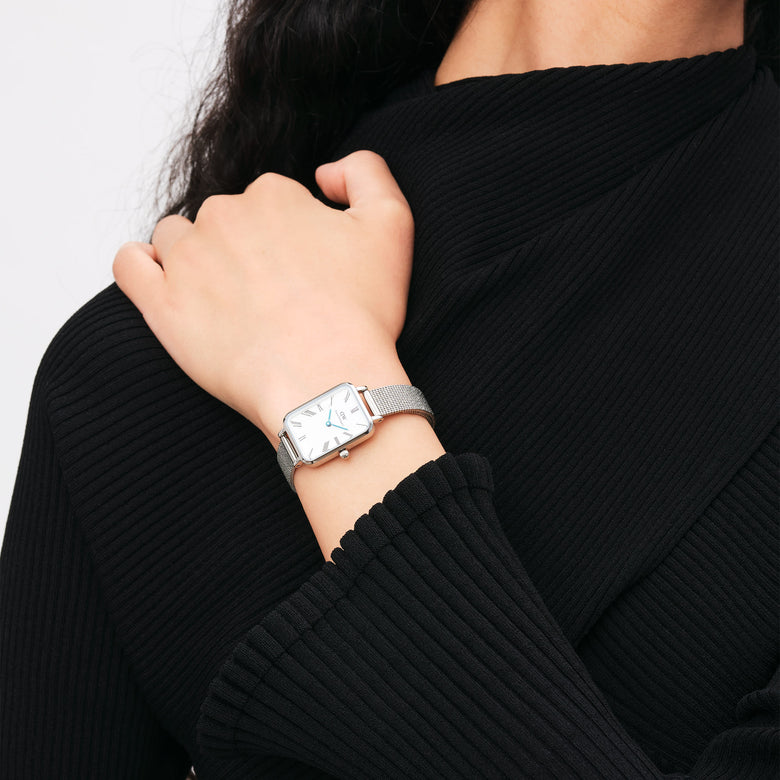 Quadro Roman Numerals Sterling ladies watch with a rectangular silver case, white Roman numeral dial, and silver mesh strap, worn on the wrist with a black ribbed top.