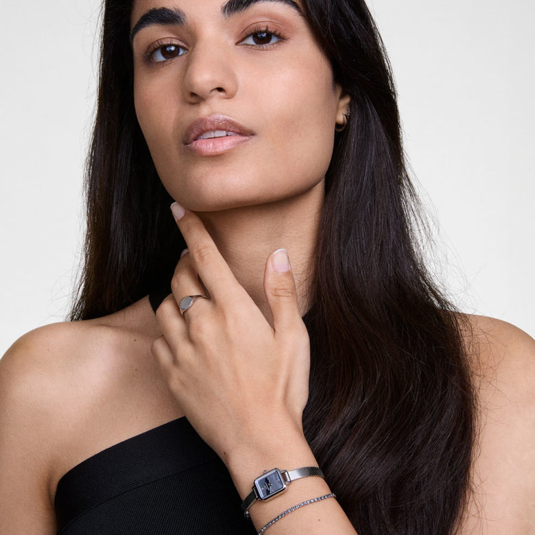 A woman wearing the Daniel Wellington Quadro Reflection watch with a rectangular silver dial and mesh strap, styled alongside the Classic Tennis Bracelet with sparkling stones for an elegant, contemporary look.