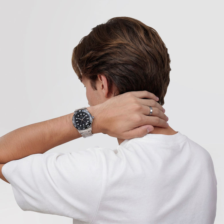 A man wearing the Iconic GMT Link Black Ceramic Bezel Silver watch, featuring a stainless steel bracelet and bold black dial, styled casually with a white T-shirt for everyday versatility.