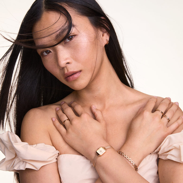 A woman wearing the Quadro Mini Melrose Champagne watch with a rose gold mesh strap, styled alongside matching jewellery and a light off-shoulder top, highlighting its petite rectangular champagne dial and elegant minimalist design.