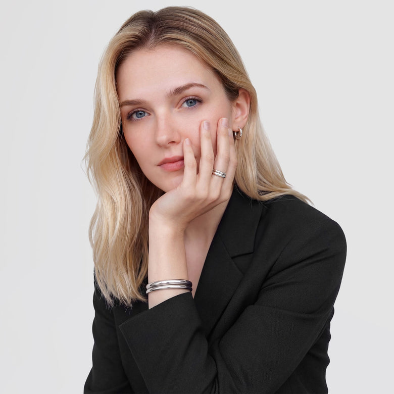 A woman wearing a black blazer showcases the Arch Ring Silver 2.5mm on her finger, styled with a minimalist silver bangle and hoop earring for a modern, elegant look.