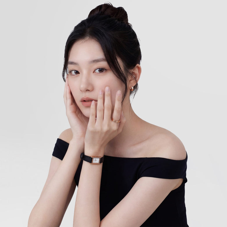 A woman wearing the Daniel Wellington Bound Mini Black Lizard Rose Gold watch, featuring a slim rectangular rose gold case, minimalist white dial, and a textured black leather strap, styled with an off-the-shoulder black top for a refined everyday look.
