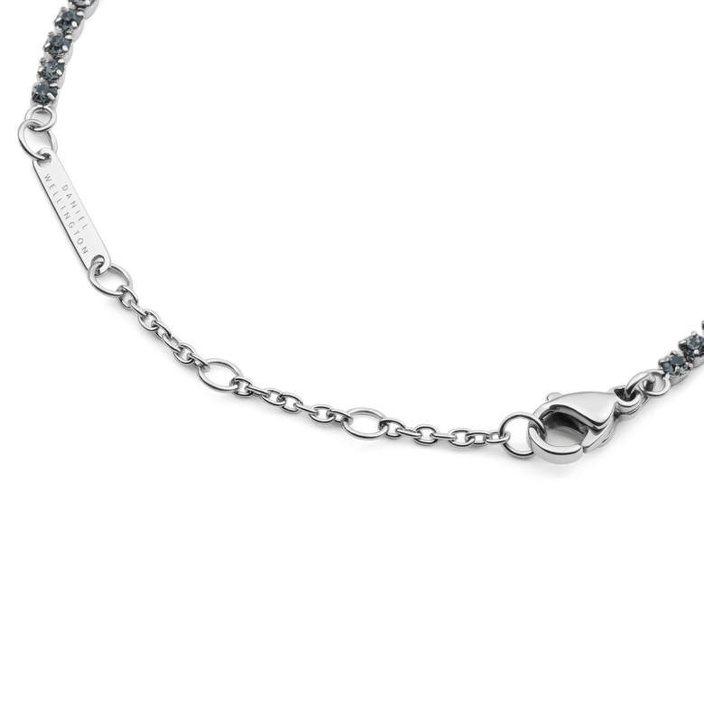 Detail of the Classic Tennis Bracelet Nightfall Silver showing the polished silver chain, secure lobster clasp, and individually set dark Preciosa crystals, with the Daniel Wellington logo engraved on the tag.