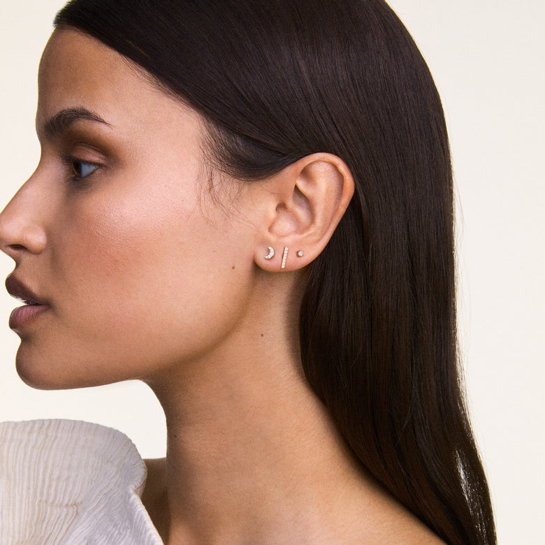 The Crystal Bar Stud Silver earring is shown worn in a curated ear stack, highlighting its slim silver bar set with seven cubic zirconia crystals for a minimalist, sparkling accent suitable for everyday wear.