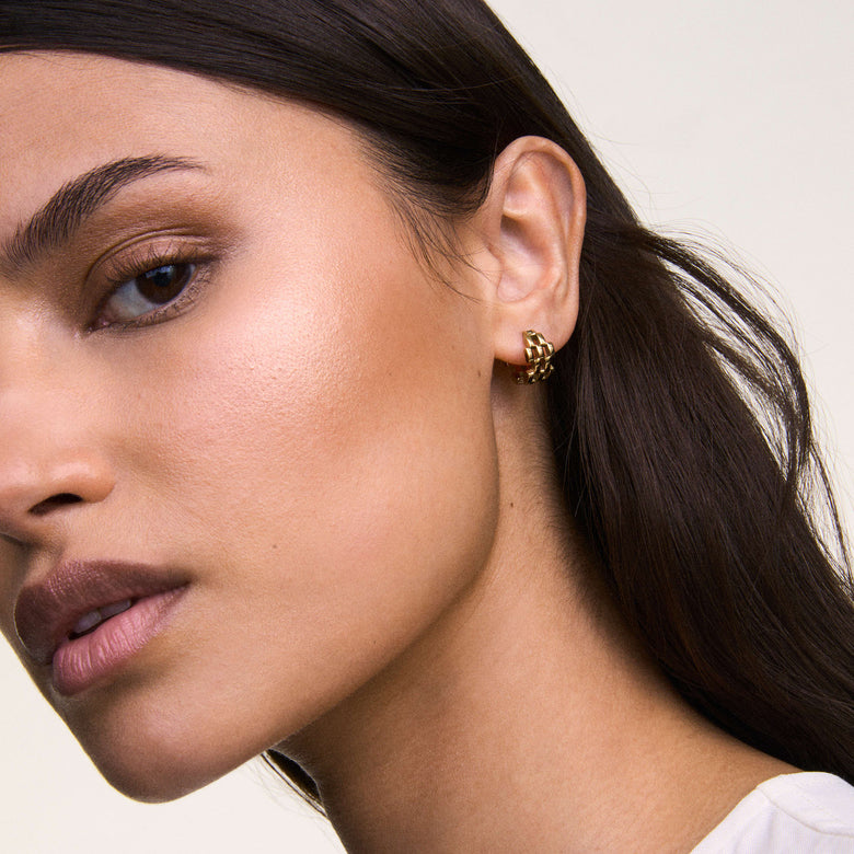 The Daniel Wellington 5-Link Earrings Gold are shown worn on the ear, highlighting their geometric open link design and polished gold finish, styled with dark hair and a white top for a modern, elegant look.