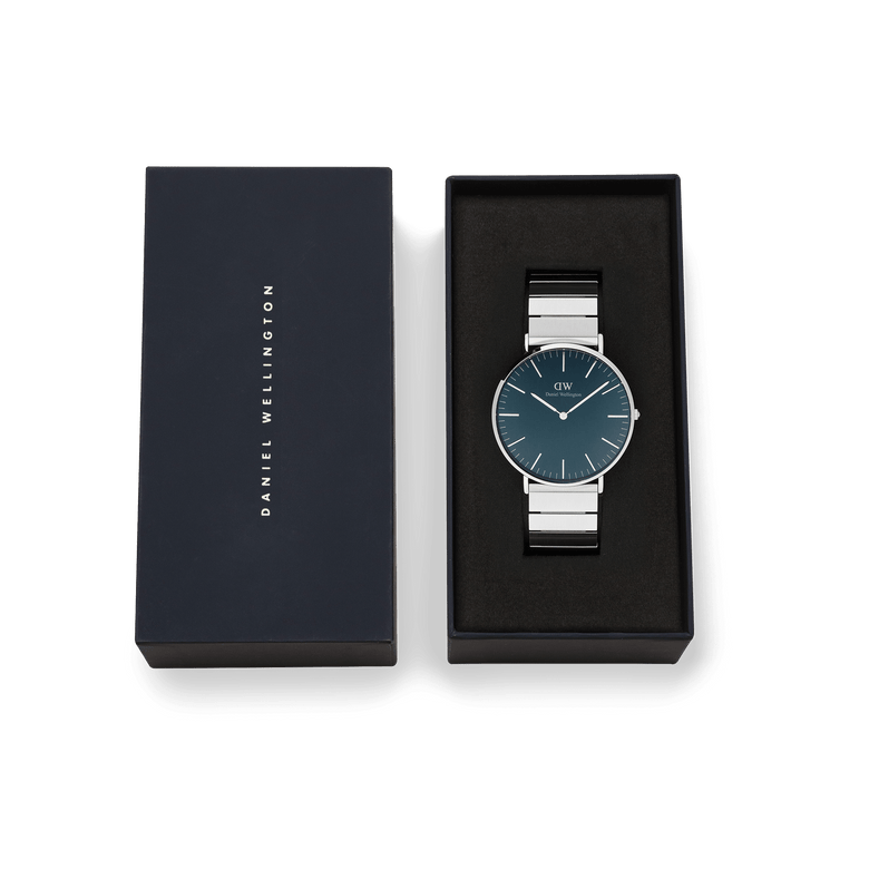 Classic Piano Link Arctic Silver watch with a brushed arctic blue dial and stainless steel piano link strap, presented in a black Daniel Wellington gift box.