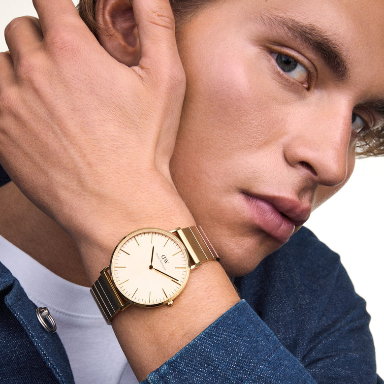 A man wearing the Classic Piano Link Gold Unitone watch, featuring a brushed gold dial and geometric piano link bracelet, styled with a casual blue shirt for a modern, refined look.