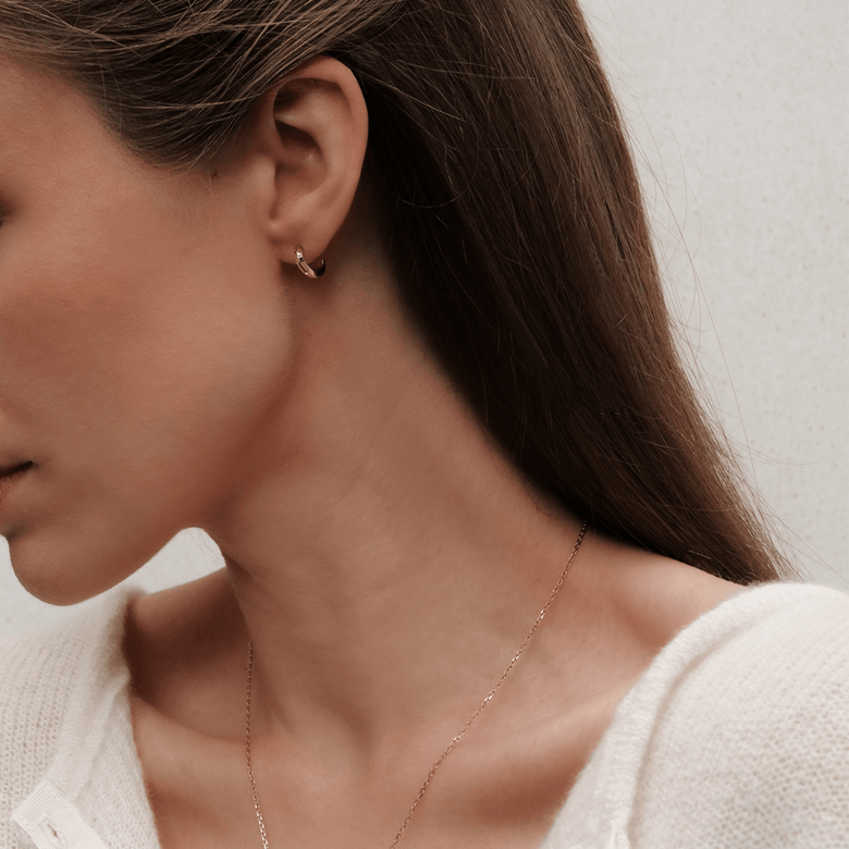 A woman wearing Daniel Wellington Elan Earrings Rose Gold, showcasing the petite huggie design and minimalist rose gold finish, styled with a delicate rose gold necklace for an elegant everyday look.