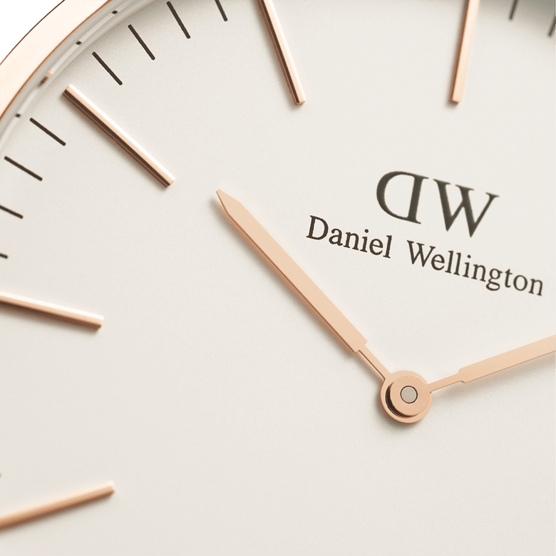 Detailed view of the Classic St Mawes Rose Gold watch face, showing rose gold hands, minimalist hour markers, and the eggshell white dial with Daniel Wellington branding.