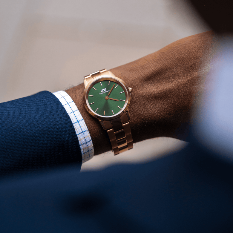 The Iconic Link Emerald Green Rose Gold watch is worn on the wrist, featuring a polished rose gold stainless steel bracelet and a striking emerald green dial, styled with formal business attire.