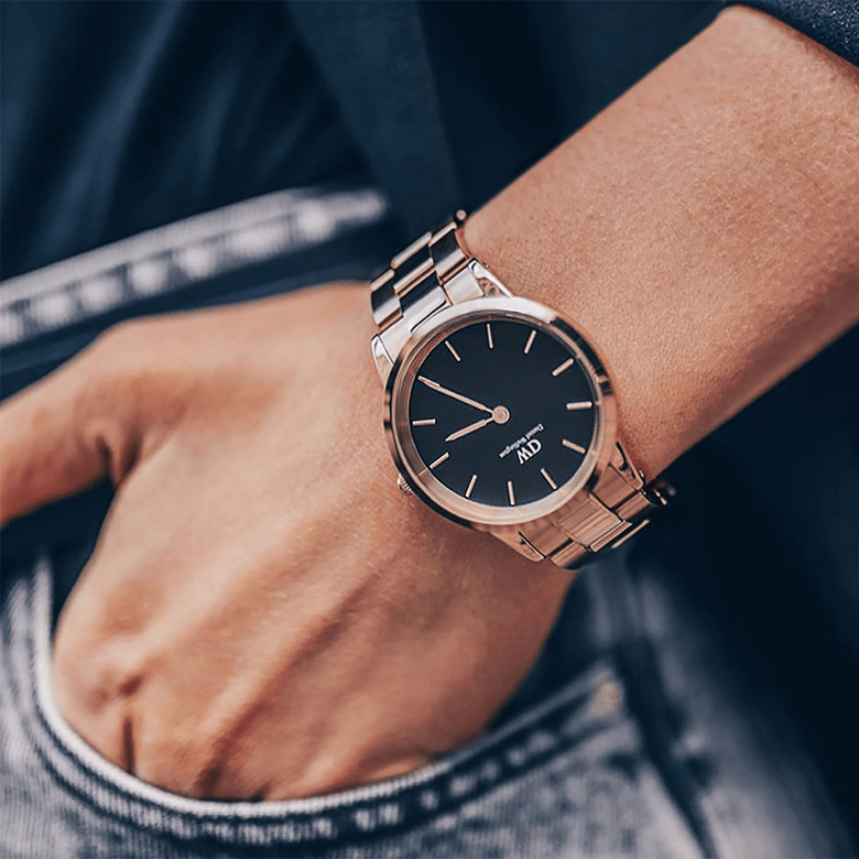 Daniel Wellington Iconic Link Black Rose Gold watch with a black dial and rose gold stainless steel bracelet, worn on the wrist with casual denim jeans and a navy jacket.