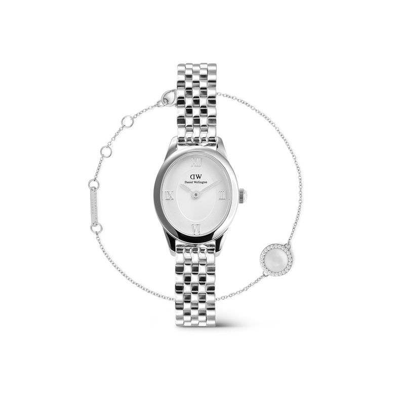 A petite oval silver watch with a polished link strap and minimalist white dial featuring Roman numerals, paired with a delicate silver bracelet accented by a mother of pearl charm and fine detailing.