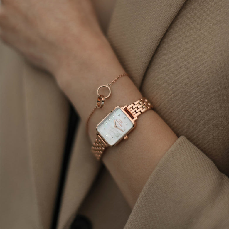 Quadro Lumine 5 Link Melrose White MoP Rose Gold ladies watch with a rectangular rose gold case and white mother of pearl dial, worn on the wrist alongside a delicate rose gold bracelet, styled with a beige coat for a sophisticated everyday look.