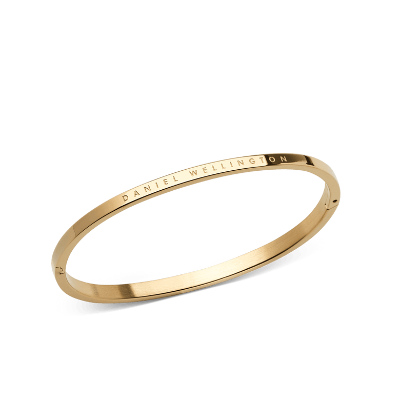 Classic Bangle Gold features a slim, minimalist design with a polished gold finish and Daniel Wellington branding engraved on the outer edge, shown at an angle to highlight its elegant profile.