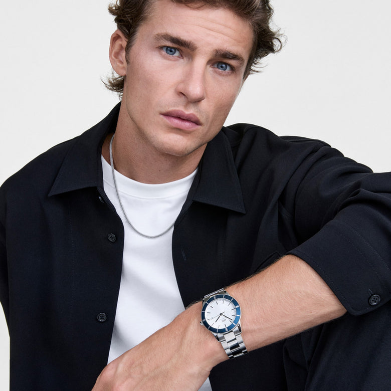 A man wearing the Iconic Paradigma Link Blue Bezel Silver watch, styled with a black shirt and white T-shirt, showcasing the bold blue bezel and silver three-link bracelet for a modern, versatile look.
