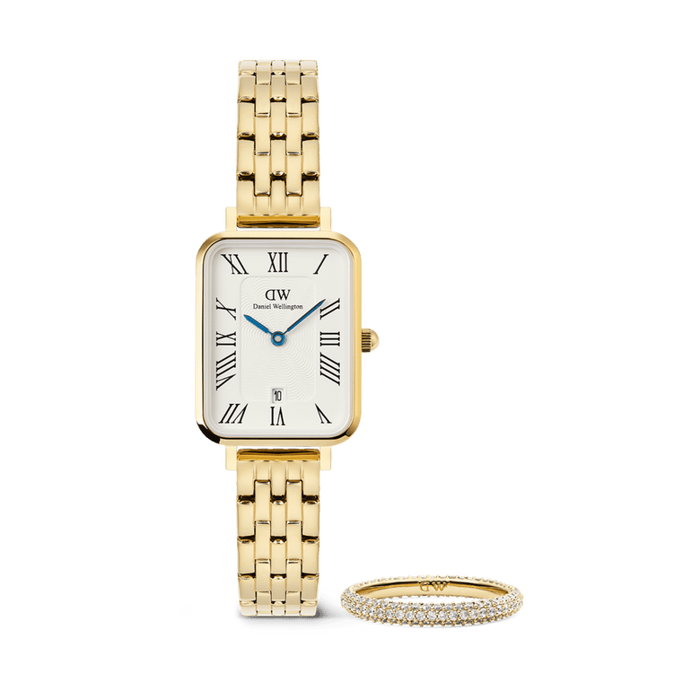 Rectangular gold women’s watch with a five-link bracelet, white dial, Roman numerals, blue hands, and date display, paired with a slim gold pavé ring set with sparkling crystals.