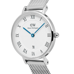 Close-up of the Petite Roman Numerals Date Silver watch showing its guilloché textured dial, blue hands, Roman numeral hour markers, date window at 6 o’clock, and slim silver mesh strap.