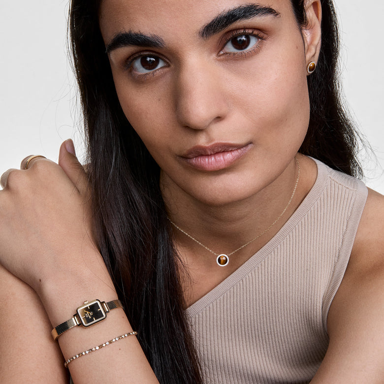 Woman wearing the Audrey Necklace Tiger Eye Gold, featuring a polished tiger eye pendant surrounded by cubic zirconia crystals on a gold chain, styled with matching jewellery and a neutral top.
