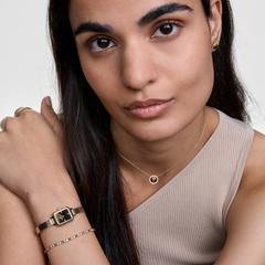 A woman wearing the Honey Gold Set, featuring a square gold mesh strap watch, a delicate tennis bracelet, and a pendant necklace with a tiger eye gemstone framed by crystals, styled together for an elegant and modern look.