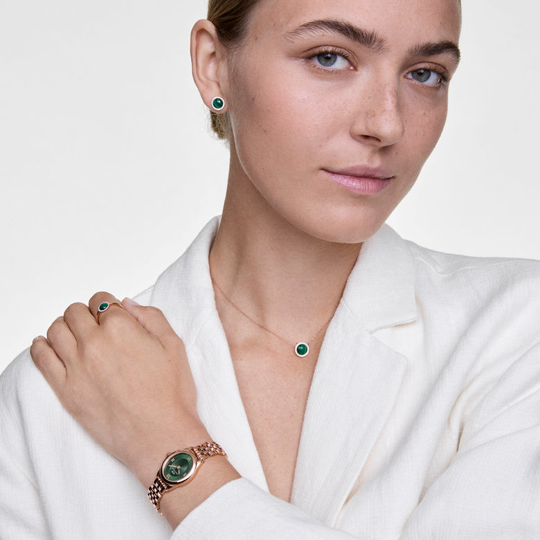 A woman wearing Audrey Earrings Malachite Gold, featuring round green malachite stones with a halo of white cubic zirconia set in gold, styled with a matching necklace, ring, and watch for a coordinated, elegant look.