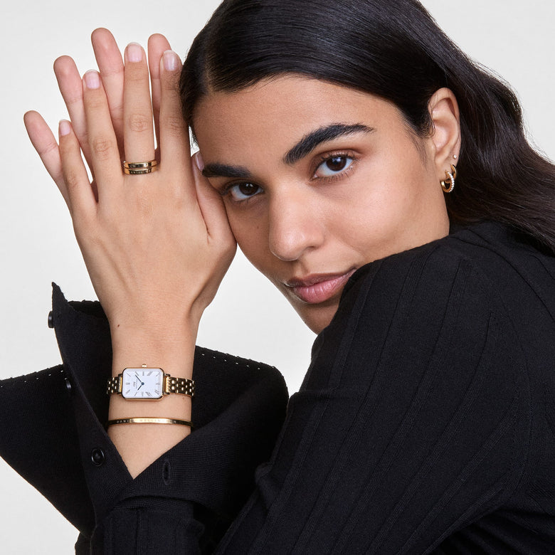 Classic Bracelet Gold styled on a wrist alongside a gold watch and matching jewellery, highlighting its slim, polished design and engraved logo as part of a modern, elegant outfit.