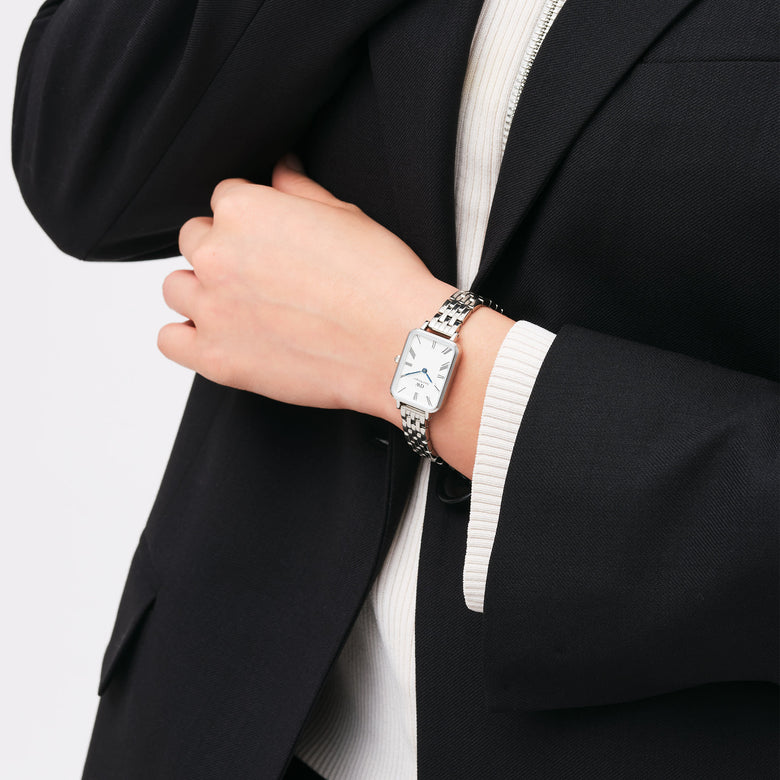 Quadro Roman Numerals 5-Link Silver watch worn on a wrist, featuring a rectangular white dial with roman numerals and blue hands, paired with a polished five-link silver strap and styled with a black blazer for a sophisticated business look.