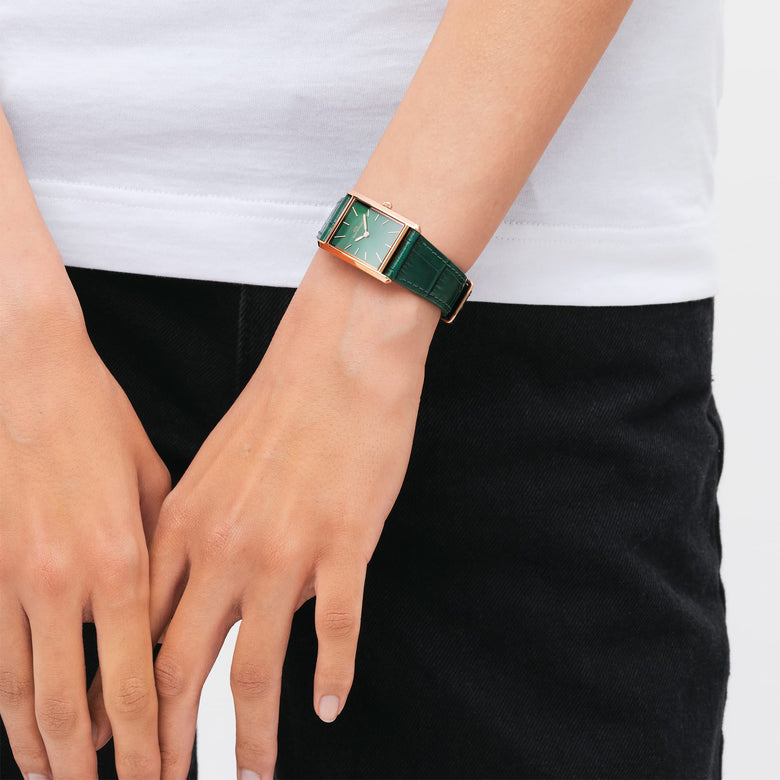Bound Crocodile Emerald Sunray Rose Gold watch with a rectangular green dial and emerald crocodile-embossed leather strap, worn on a woman's wrist with a casual white top and black trousers.
