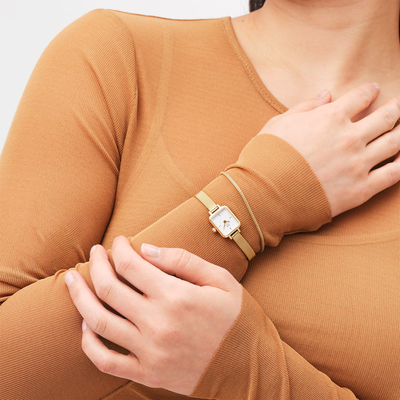 A woman wearing the Tide Mesh Bracelet Evergold 1.8 alongside a gold mesh watch, showing the slim gold bracelet’s delicate mesh texture and refined styling paired with casual attire.