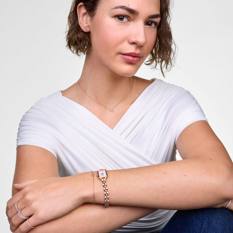 Woman wearing the Mirelle Heart Bracelet Gold with a delicate open heart charm and cubic zirconia crystals, styled alongside a gold watch and other minimalist jewellery for a polished, modern look.