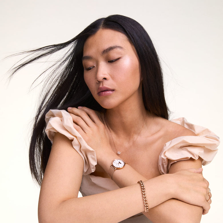 A woman wearing the Crystal Zodiac Chain Necklace Rose Gold with a Cancer zodiac pendant, styled with a rose gold watch and bracelet for an elegant, coordinated look.