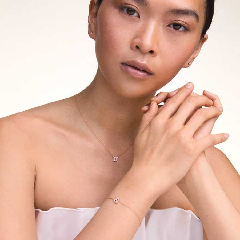 A woman wearing the Crystal Zodiac Chain Bracelet Rose Gold on her wrist, showcasing its delicate rose gold chain and sparkling zodiac pendant, styled with a matching zodiac necklace for a coordinated, elegant look.