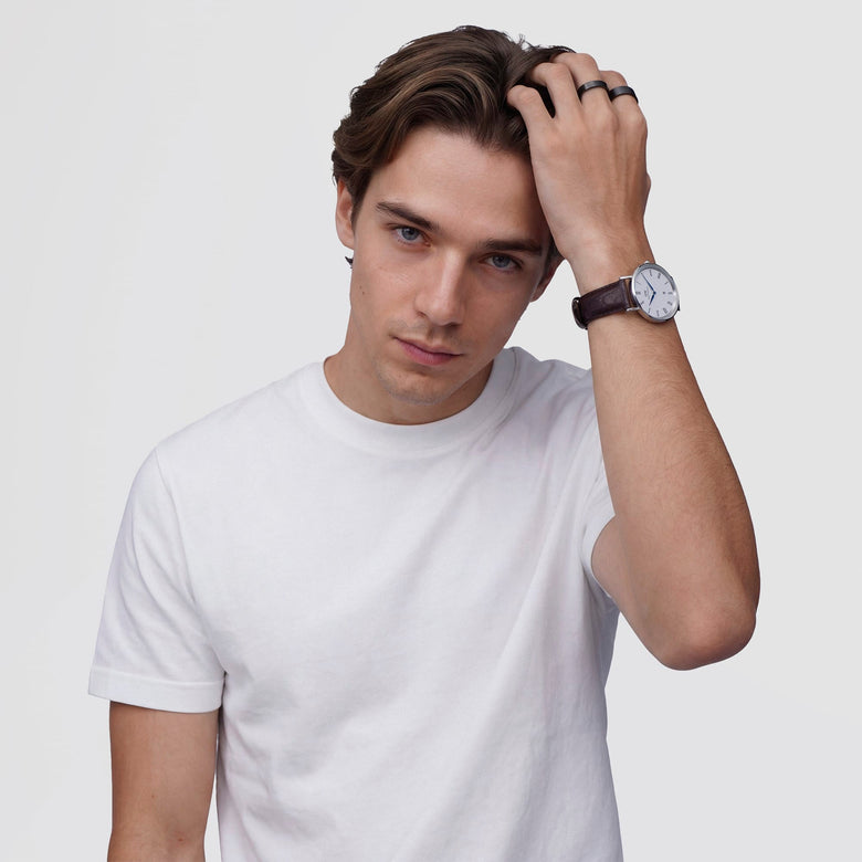A man wearing a white t-shirt showcases the Classic Roman Numerals Date Dark Brown Croc Belly Silver watch on his wrist, highlighting the elegant silver case, white dial with Roman numerals, and dark brown crocodile-embossed leather strap in a casual setting.